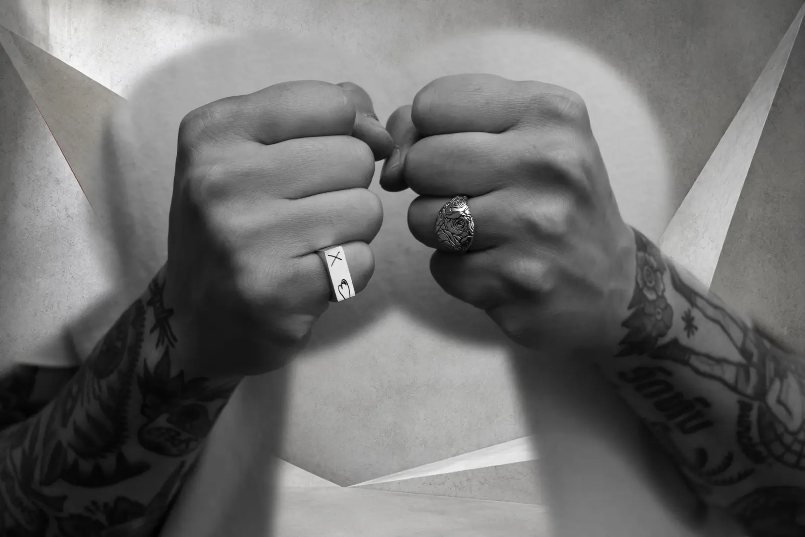 Tattooed fists wearing Matti XXX and Rose Signet sterling silver rings against a sculptural concrete setting